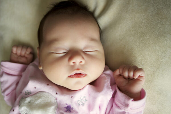 close up of baby sleeping on back in pink jumpsuit - how important is a bedtime routine for a baby?