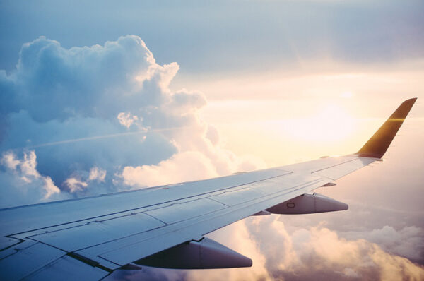 wing of plane in the clouds ; book your own flight or use a travel agent?
