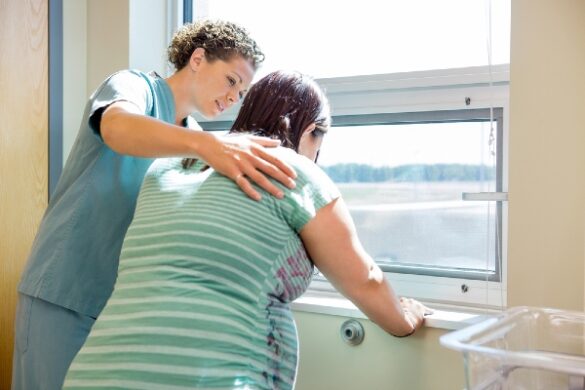 pregnant woman in labor tensed at the window receiving support from a nurse