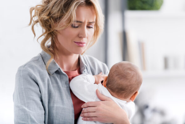 Tired mom holding fussy baby for article sleep regression ages